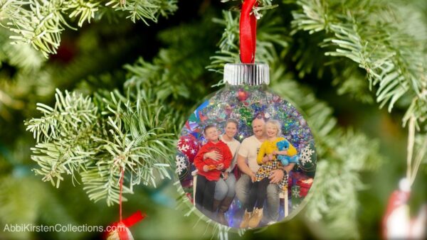 The image shows a floating Christmas ornament hanging on a tree with a family photo inside. 