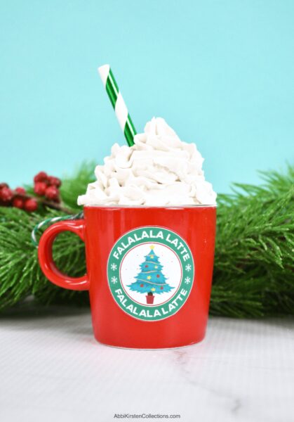 A red mini coffee cup ornament with a Christmas tree coffee sticker label. Spackle creates a frothy mug look with a green and white paper straw. Get the free printable Christmas stickers at Abbi Kirsten Collections.