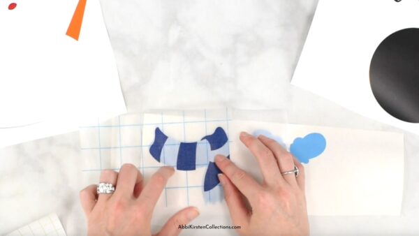 Abbi Kirsten's hands show how to use parchment or butcher's paper to align the scarf layer on the seasonal sign. 