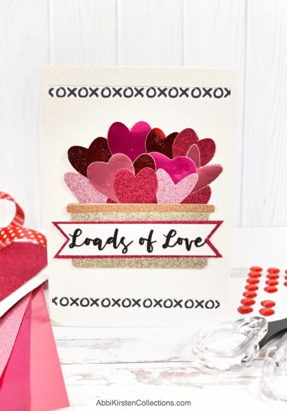 A DIY Valentine's Day card with the phrase "Loads of Love" and hearts in a basket. The card is cut out with a Cricut machine. 