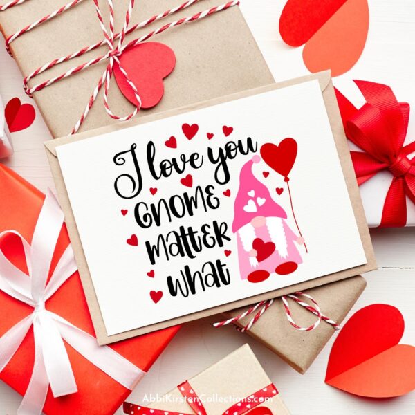 A hand-made card with a female gnome on the cover and the words "I love you gnome matter what" lays on red and tan wrapped Valentine's Day presents. 