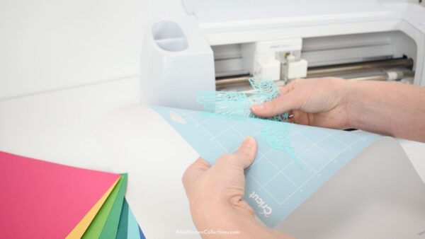 The image shows how to remove delicate cardstock cutouts from a Cricut mat. 