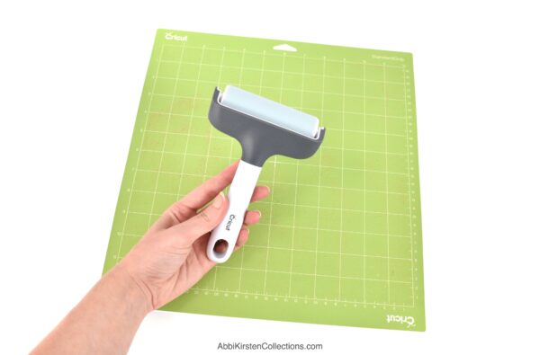 The image shows a green Cricut mat with a Cricut brayer tool used to press materials to the mat for the best cutting results. 