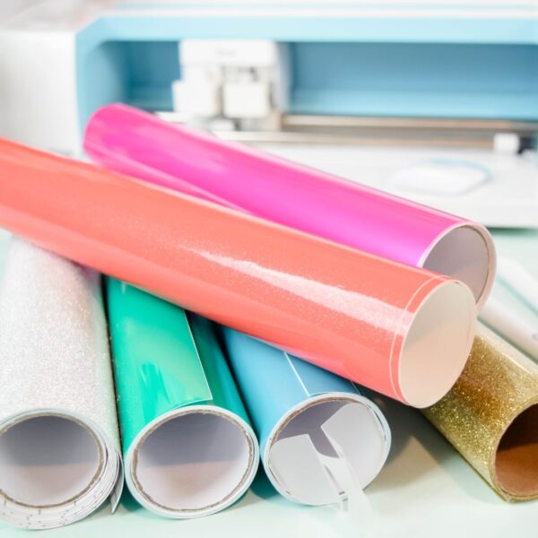 Colorful rolls of craft vinyl on a desk with a Cricut in the background