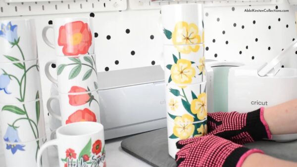 Still wearing heat-safe gloves, Abbi Kirsten stacks the final mugs with the flower designs next to the other two mug stacks with other flower sublimation presses. 