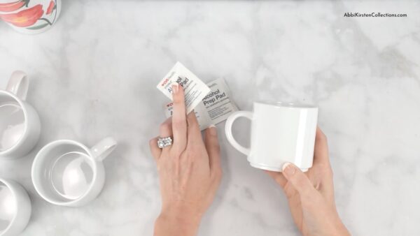 A bird’s eye view of Abbi Kirsten’s hands as she prepares the sublimation mug blanks using rubbing alcohol. 