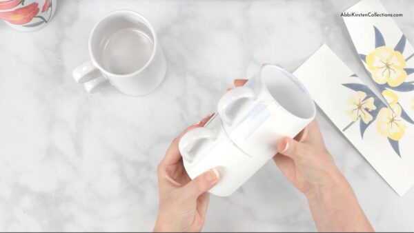 Abbi Kirsten holds two blank mugs together to ensure the stackable mug design will line up correctly. Two pieces of the yellow flower design lay to the right. 
