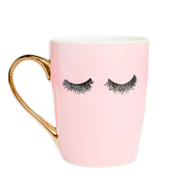 A pink coffee mug with a gold handle and a set of drawn-on feminine eyelashes on the front.