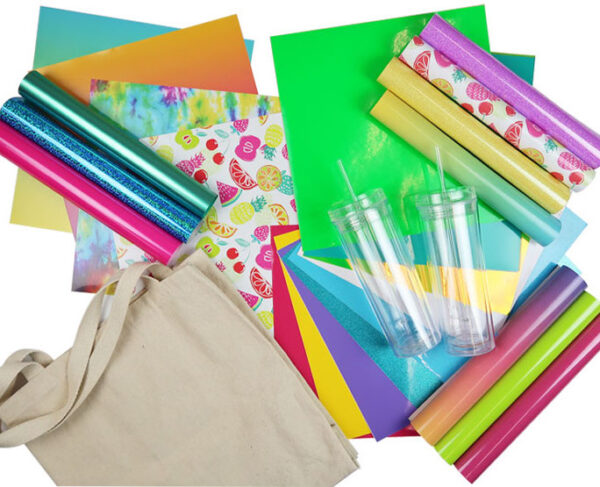 An overhead view of crafting supplies on a white surface. Supplies include multiple colorful vinyl rolls, a beige bag and clear rolls.