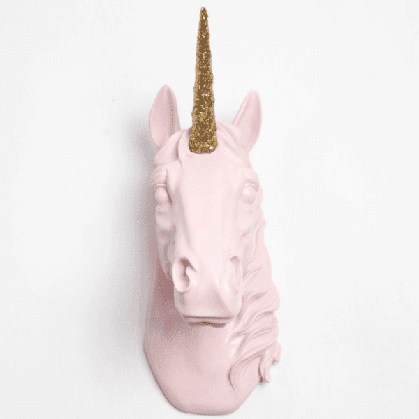 A wall mounted pink unicorn head with a glittery gold horn hangs on a white wall.