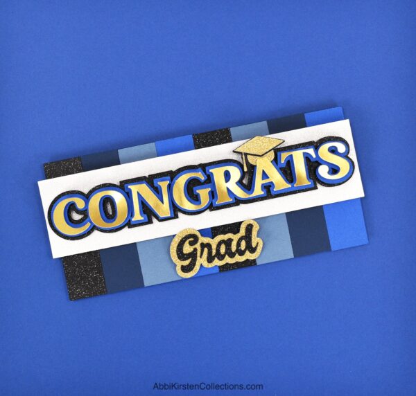 The image shows a congrats grad card in blue, black and gold. You can make these layered Cricut cards using the templates found in the member's section. 