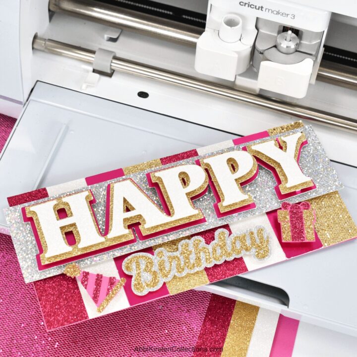 The image shows a pink and gold happy birthday card made with a Cricut machine. Learn how to make cards with Cricut.
