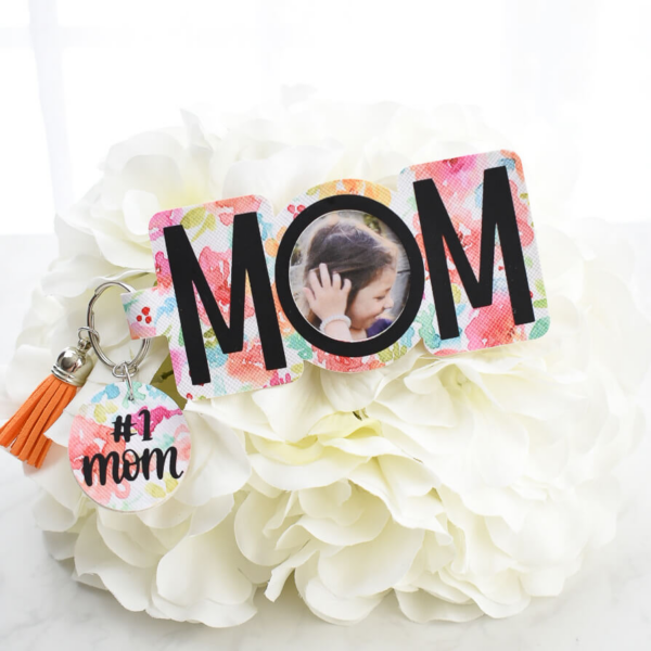 The image shows a DIY photo keychain made from colorful floral faux leather with a personalized picture that says Mom. 
Get the free SVG file. 