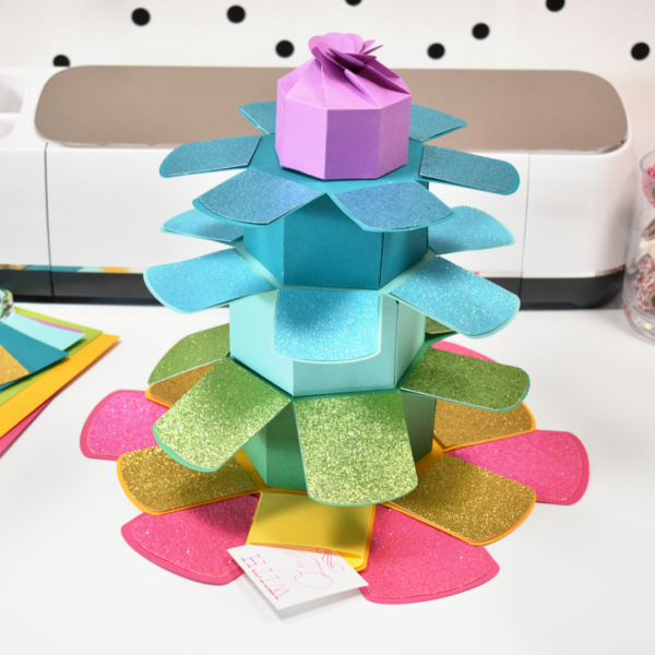 The image shows a DIY tower explosion gift box in rainbow colors made with a Cricut machine. Get the free gift box SVG templates on Abbi Kirsten Collections.