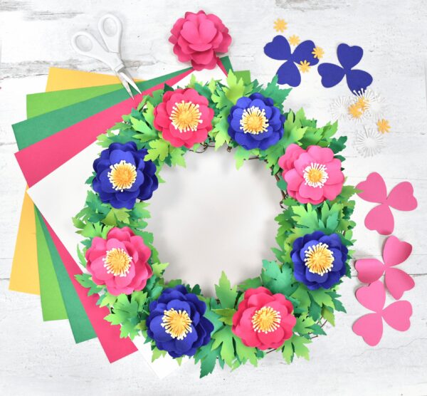The image shows a spring wreath made from paper. Get creative with this fun springtime project! Learn how to make a stunning paper flower primrose wreath using your Cricut.