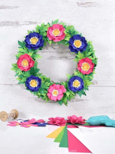 The image shows a pink, purple and green spring wreath. Looking for a fun, creative way to spruce up your front door this spring? Learn how you can make a beautiful paper flower primrose wreath with the help of our simple DIY tutorial and your Cricut machine!