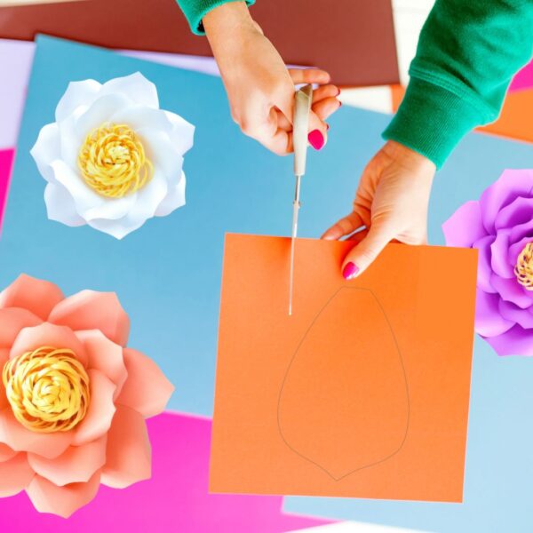 The image shows a crafter cutting cardstock paper with scissors to make paper flowers
