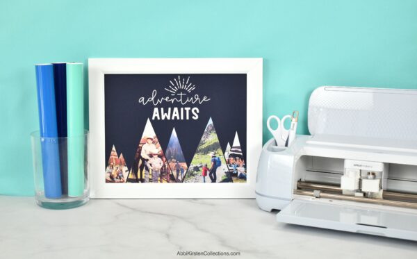 This image shows a Cricut machine with vinyl and a finished project of a frame that says, Adventure Awaits with a mountain range with personal travel photos inside. 