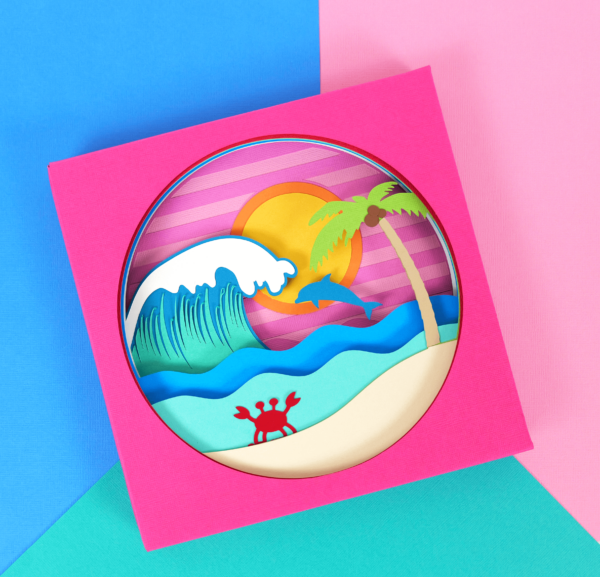 Layered shadow box with a beach scene and dolphin made from cardstock paper. 