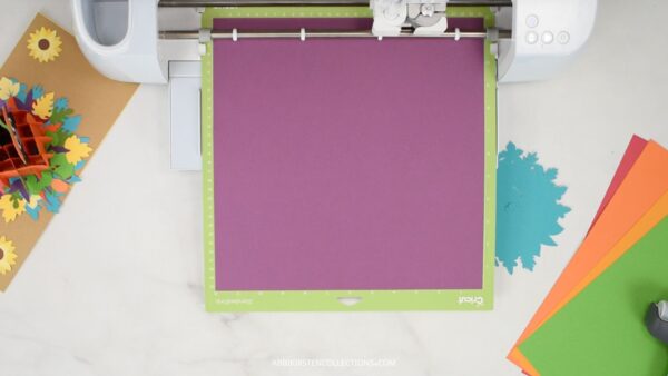 Purple cardstock being cut out on a Cricut machine. 