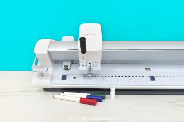 Cricut Venture on a white desk with large marker pens in clamp A. 
