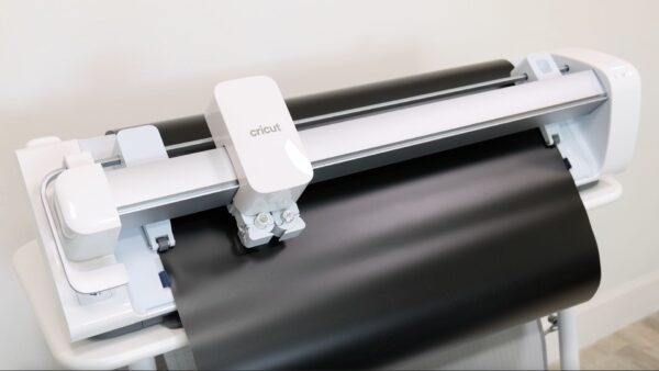 The Cricut Venture machine on a docking stand cutting our black smart vinyl. 