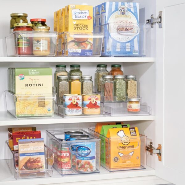 Clear pullout bins hold dry good and cans, neatly organized in an open white pantry cabinet. 