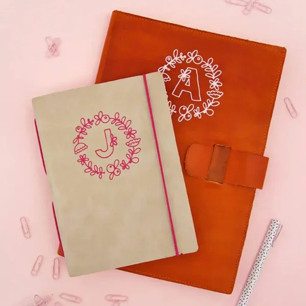 Beige notebook with letter J monogram and rust-colored notebook with letter A monogram. 