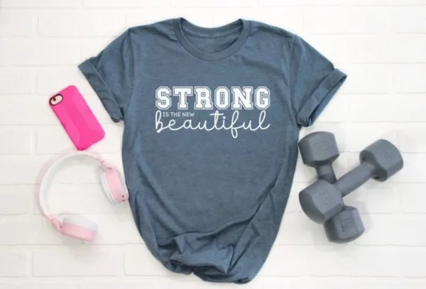 Offering free SVG files for Cricut with this gray t-shirt and white text Strong is the new beautiful, pink cellphone and headphones, and two small hand gray hand weights.