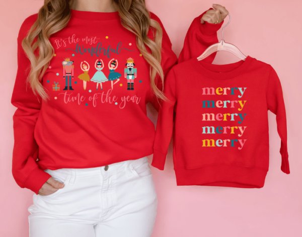 Girl wearing long-sleeve red Christmas sweatshirt with nutcrackers and ballerinas and text It's the Most Wonderful Time of the Year, holding child's shirt with text merry 5x 
