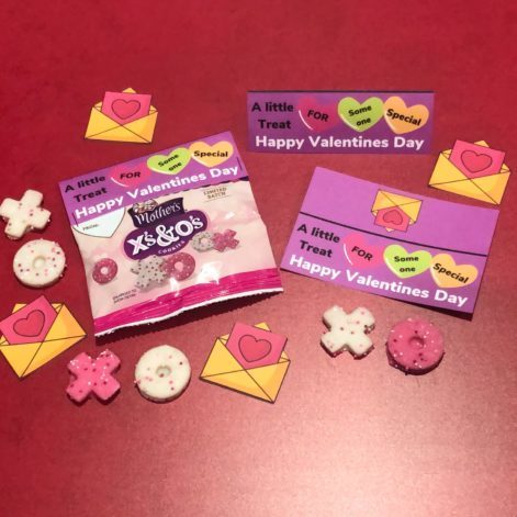 Valentine treat bag with treat topper craft surrounded by candies and min-valentines.