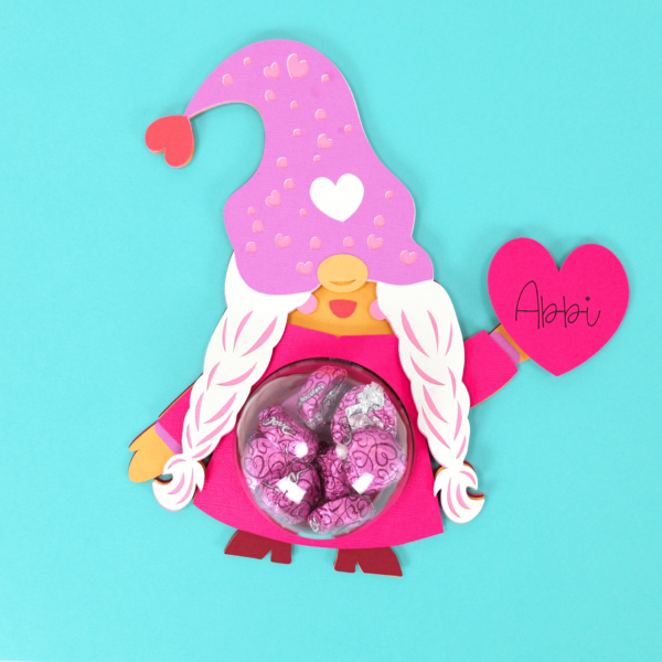 Cute girl gnome candy holder craft in pink and purple with chocolate candies in a plastic dome holder for Valentine's Day.