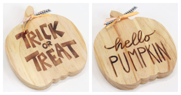 Two wooden pumpkins with stenciled text Trick or Treat and Hello Pumpkin and orange and black bows on stems.