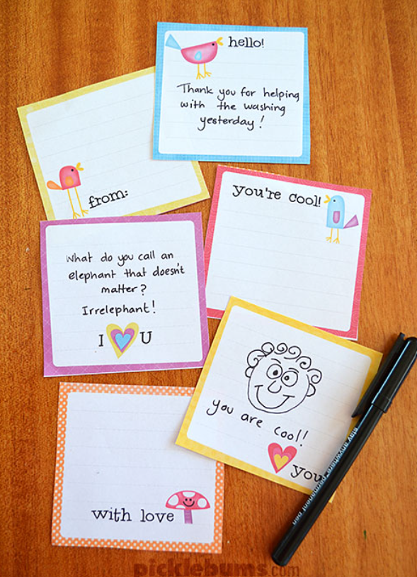Image alt-tag: Square lunch box notes are seen on a wooden table with a black pen. These free printable lunch box notes are blank and can be customized to your child or spouse. They all have a colored border and small illustrations of birds, hearts, and mushrooms. These drawings are accompanied by small phrases like "With Love" and "Hello."