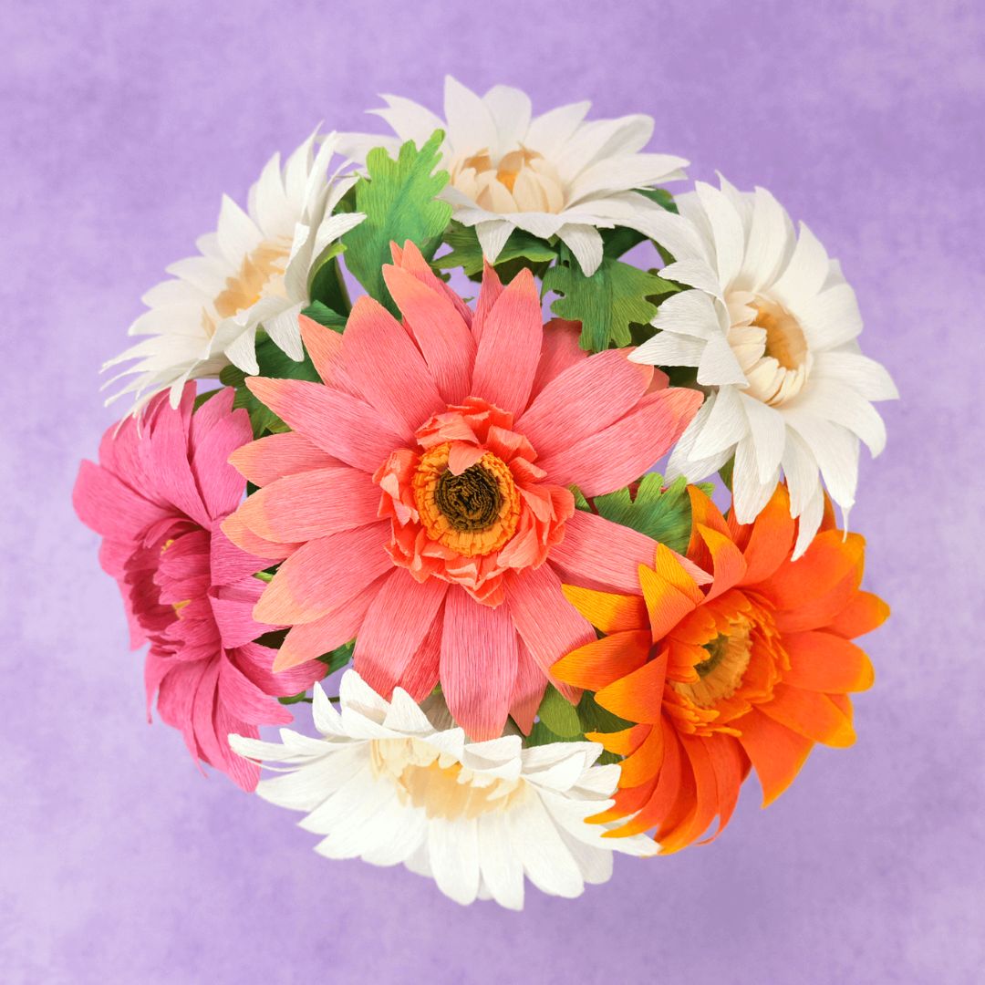 Crepe paper daisies in a white shallow vase.