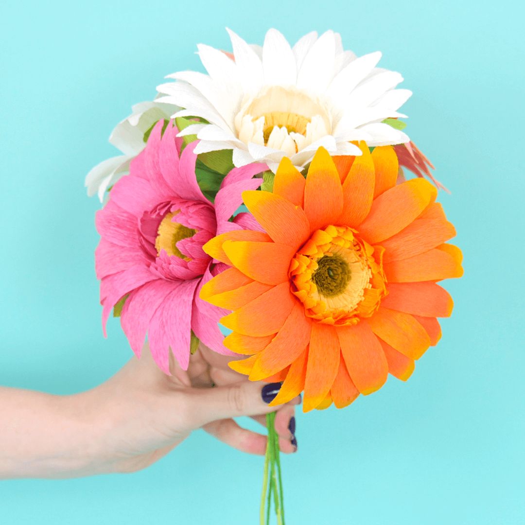 Bright crepe paper daisies being held by a woman's hand