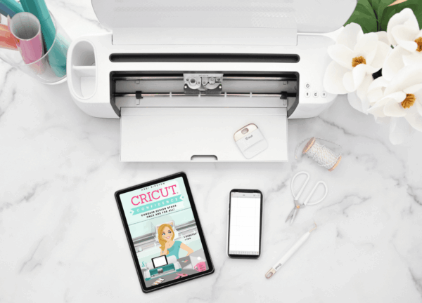 Cricut Confidence ebook on an iPad next to a Cricut, phone and craft supplies
